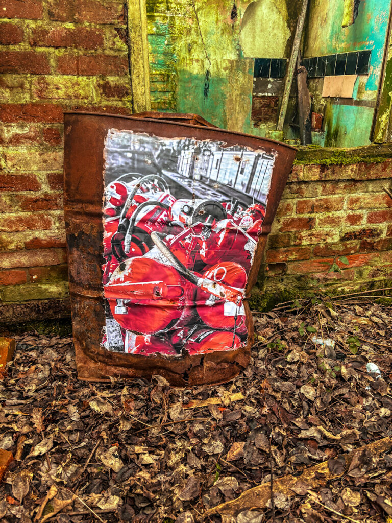 A weathered, corroded barrel with a rusty appearance, showcasing a photograph of a pile of fire extinguishers stuck to the side. The photo is weathered and rusted