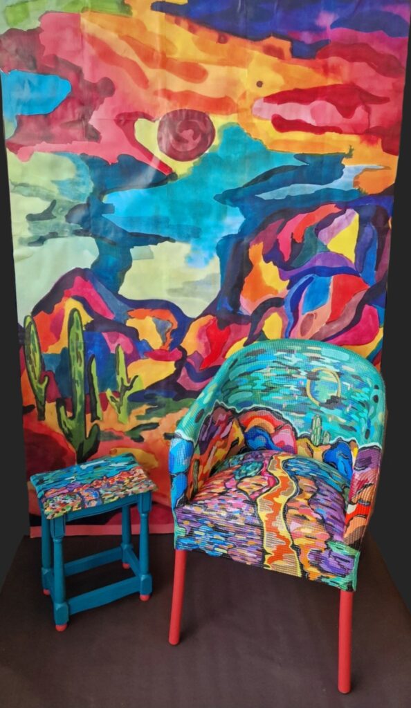 A vibrant chair and stool adorned with a colorful painting of a desert. 
Behind them is another colourful painting of desert landscape