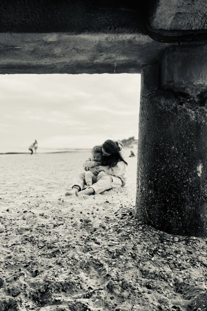 A black and white photograph of a mother and her child sitting on a beach