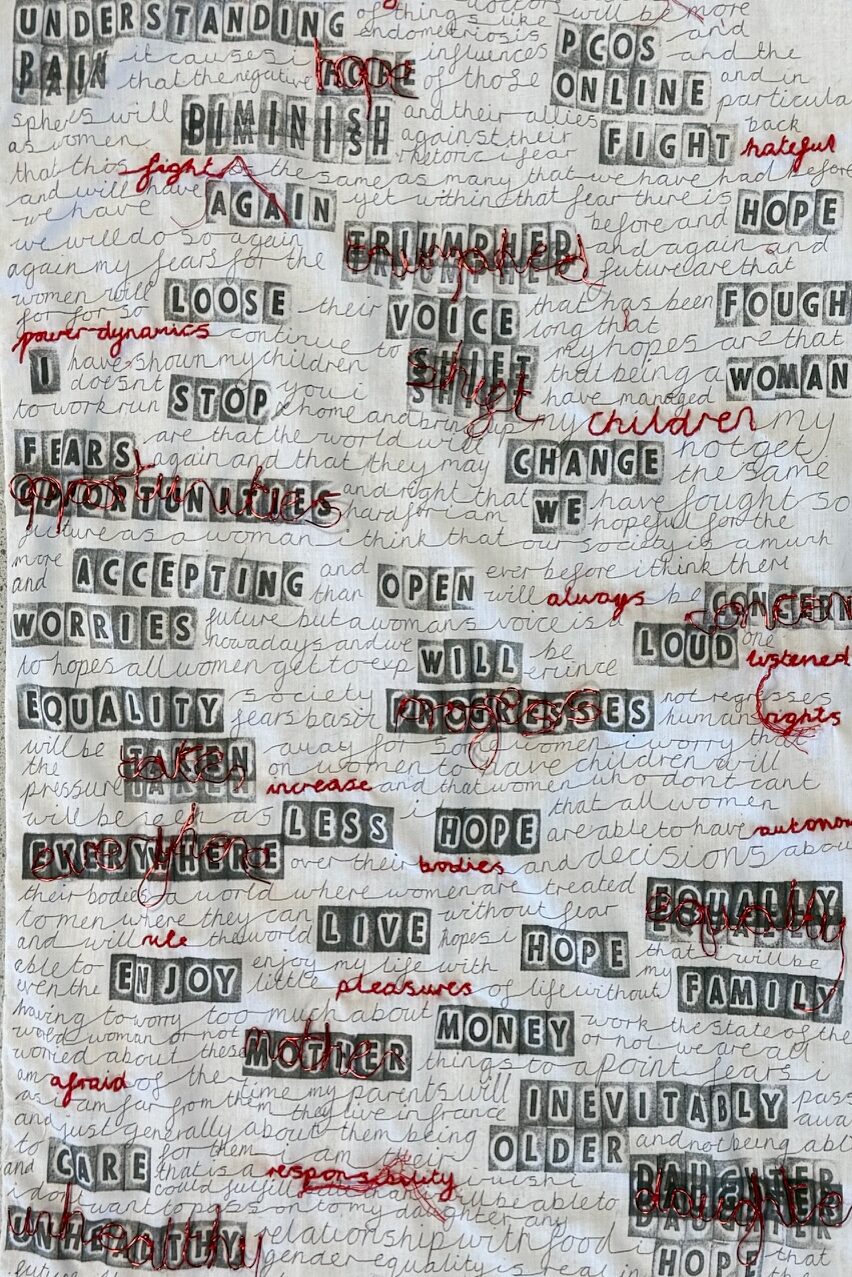 A stitched textile panel featuring embroidered and collaged words over handwritten text.