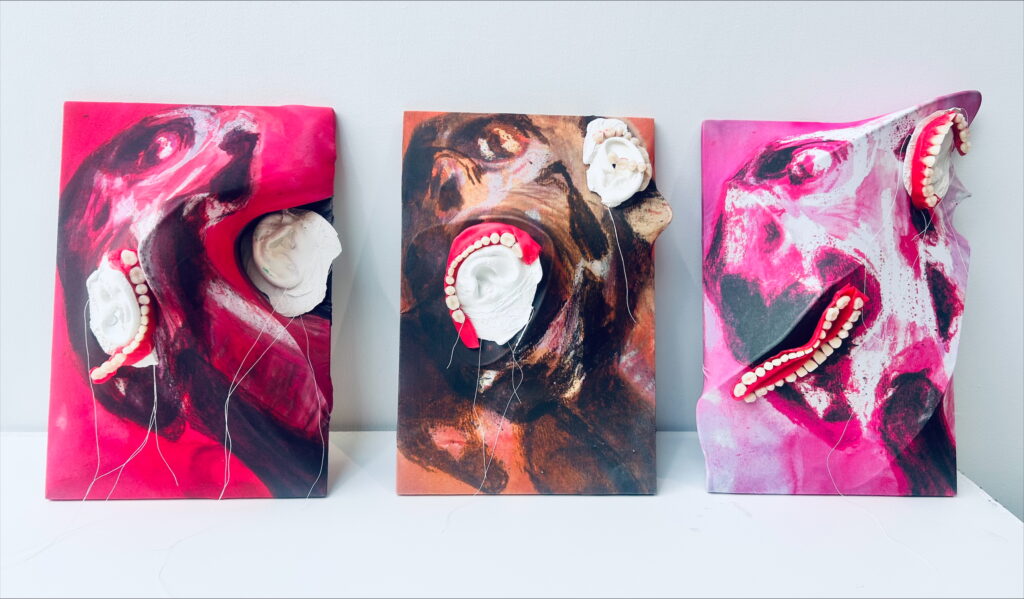 Three sculptural portraits on brightly painted panels, featuring exaggerated facial expressions with added teeth and ears made from mixed media.