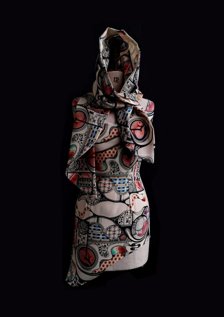 A fashion photograph showing a draped garment on a mannequin, crafted from a digitally printed fabric with detailed, abstract patterns in red, blue, black and cream tones