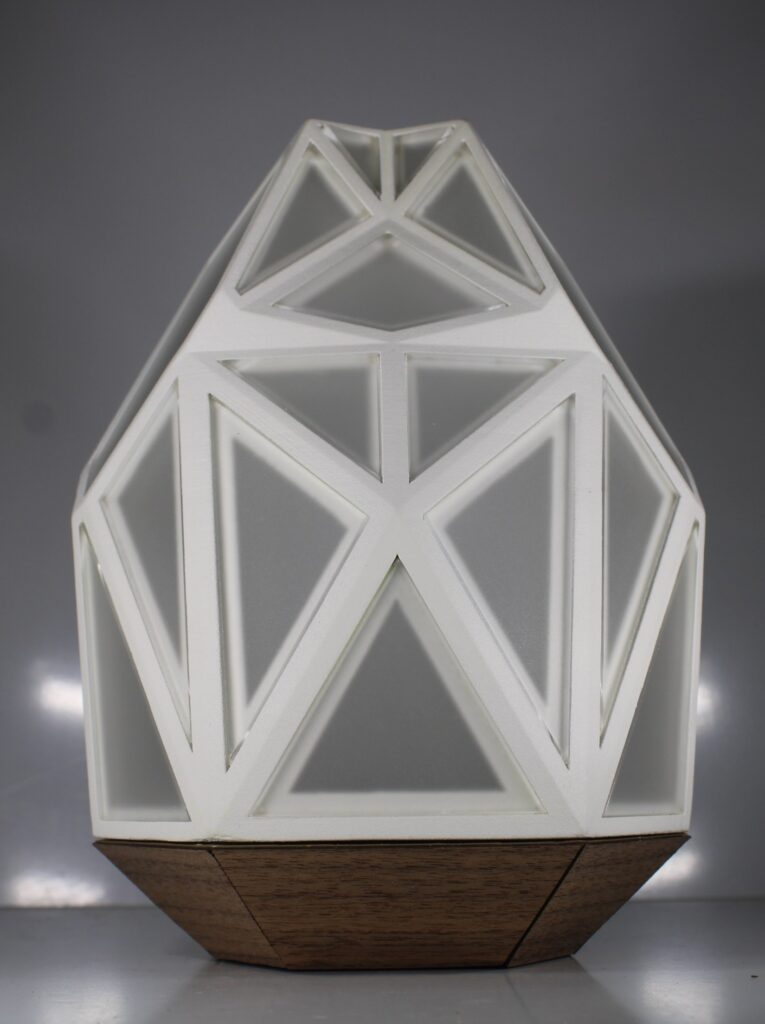 A 3D printed lamp with geometric panels and frosted surfaces, combining a white patterned body with a darker wooden base.