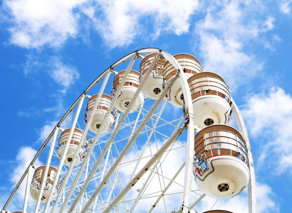 A digital photograph of a ferris wheel taken from below, showing the structure and sky on a bright day.